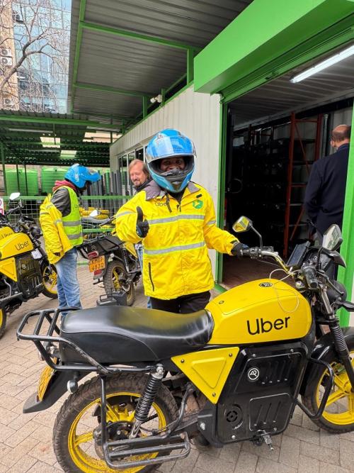 Delivery rider in yellow jacket and blue helmet beside yellow Uber-branded motorcycle in garage